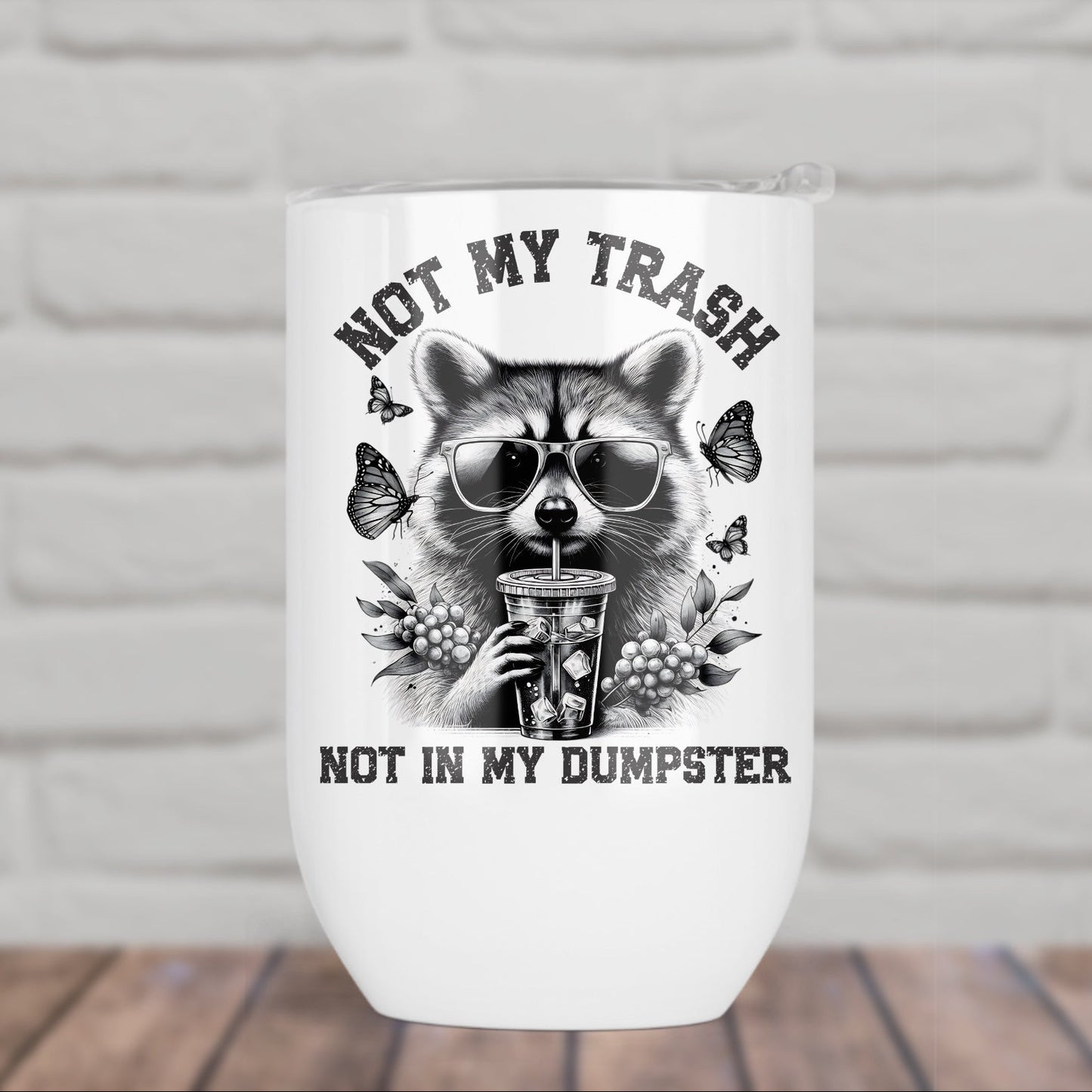 White tumbler with a raccoon design and text 'Not my trash, not in my dumpster' on a white brick background.